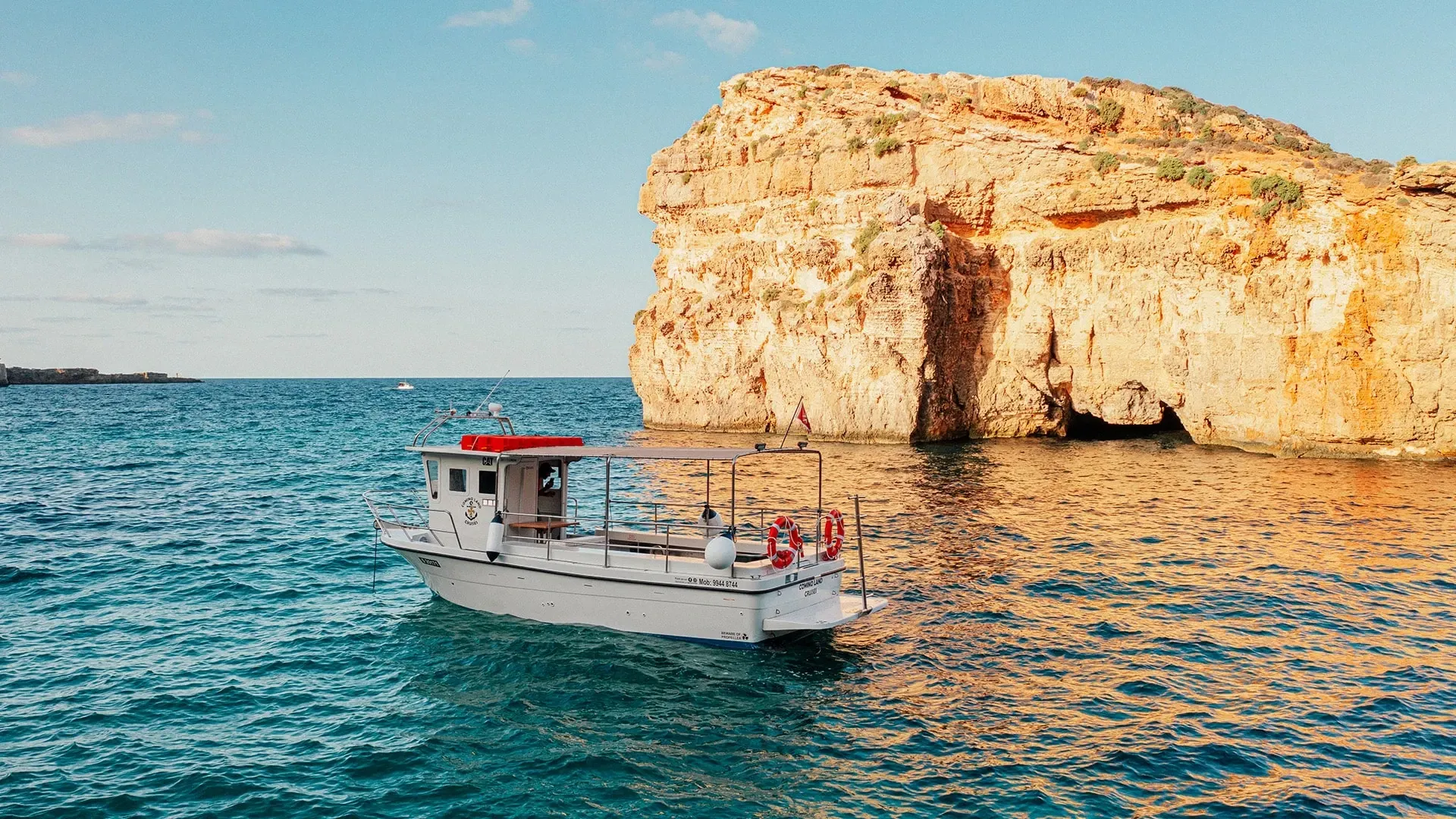 The Comino Land boat alongside limestone cliffs