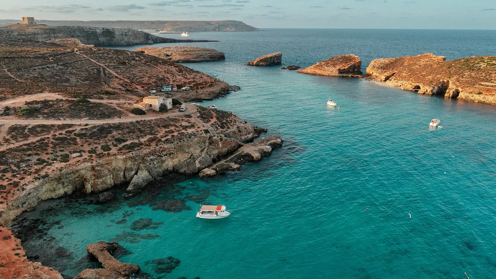 Aerial view of clear water beside Comino’s rocky coast
