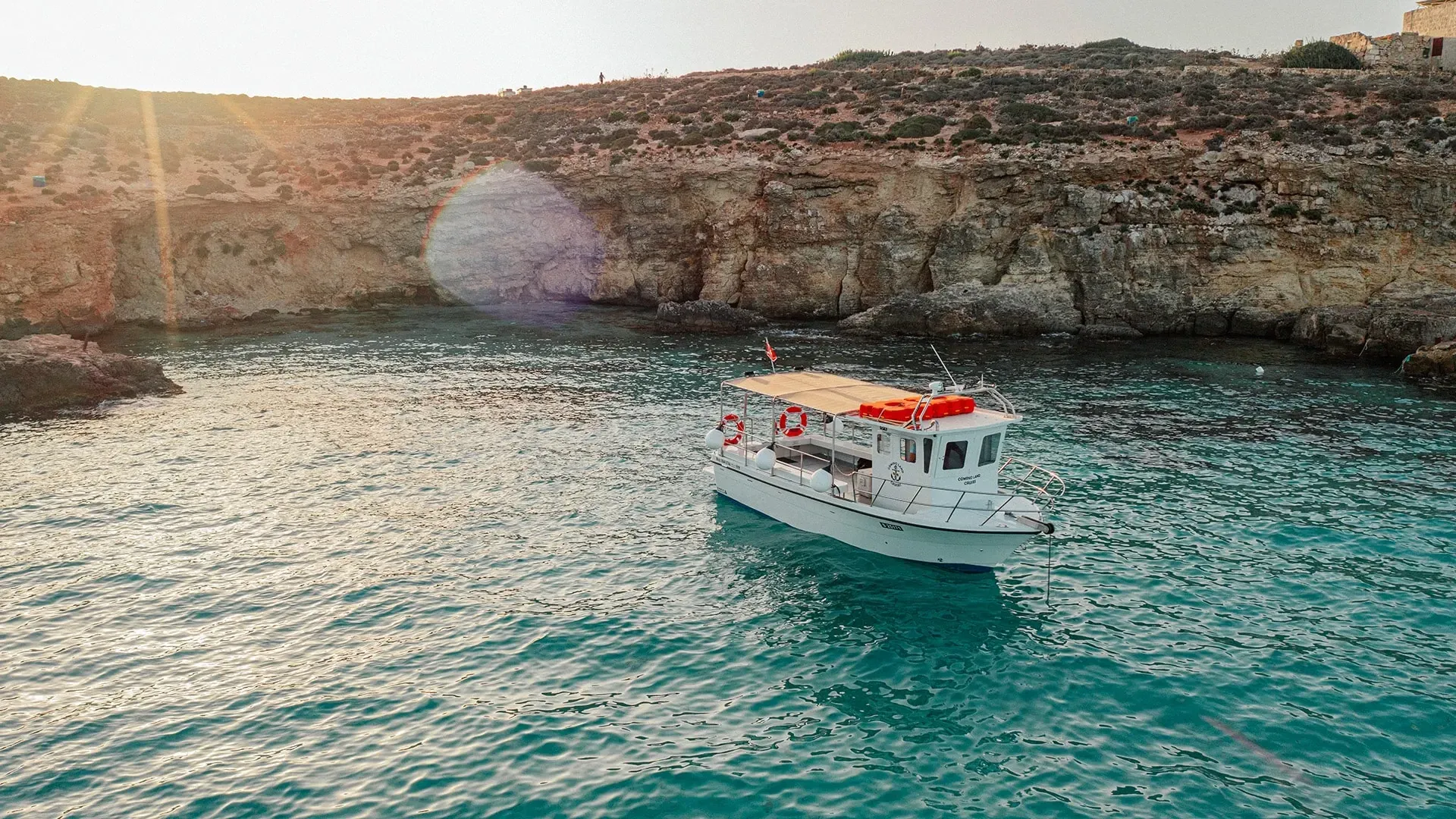 Comino Land boat beside the limestone coast in turquoise water